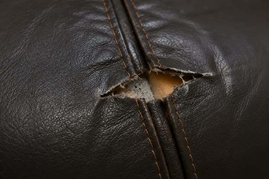 A split seam on a dark leather booth with the foam showing