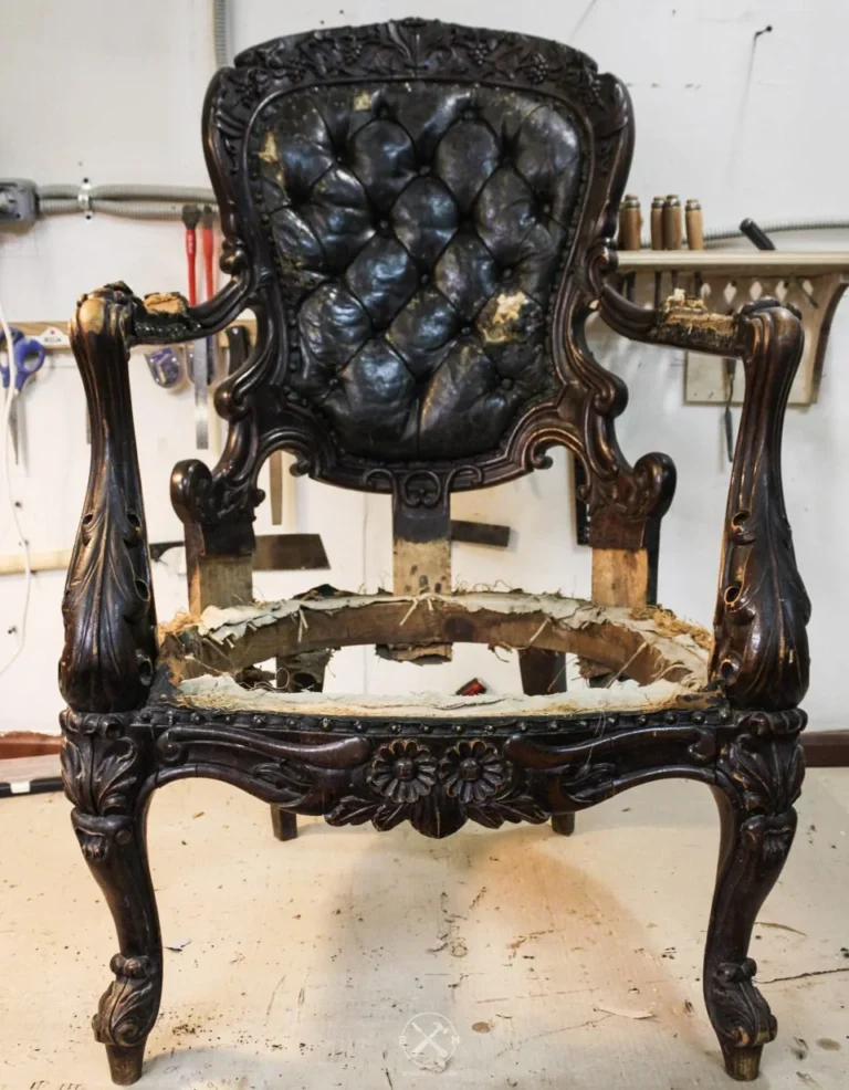 A carved wood armchair with torn tufted leather, stripped for reupholstery